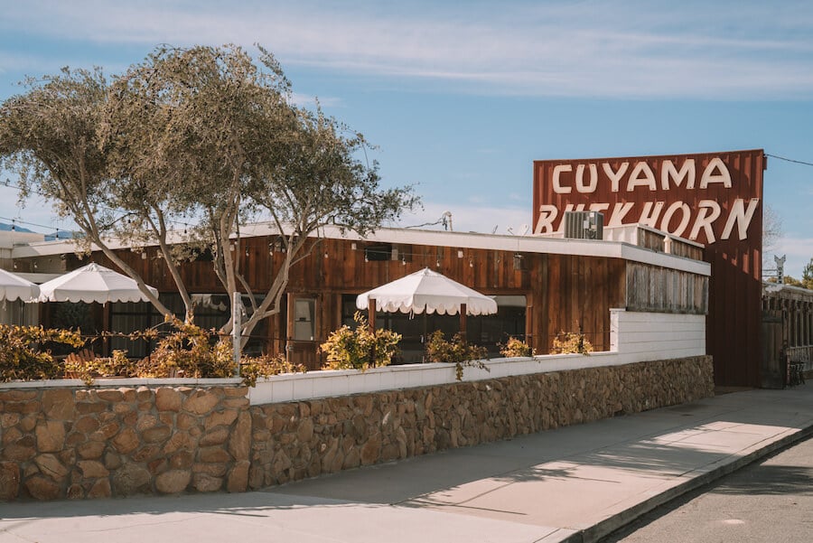 Exterior de Cuyama Buckhorn con letrero retro y sombrillas en el porche
