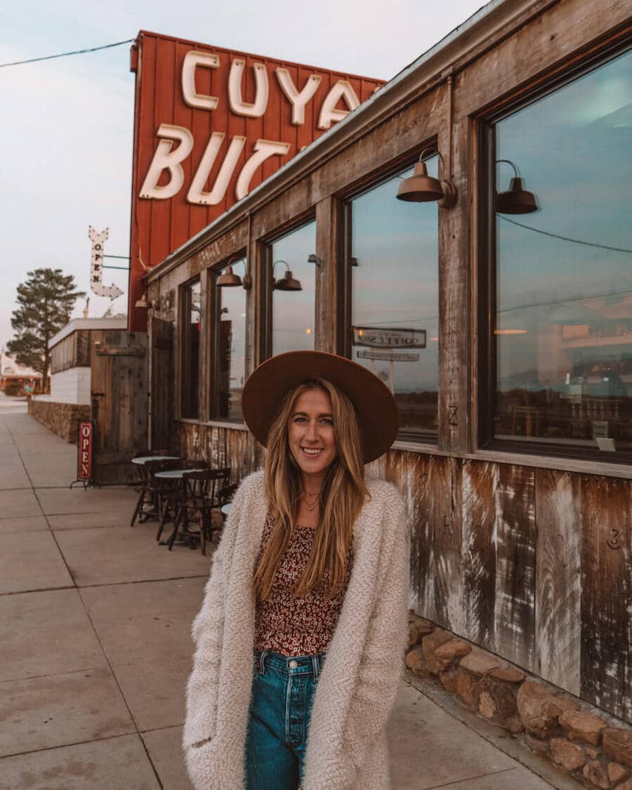 Exterior del Cuyama Buckhorn con carteles retro y una chica parada al frente con sombrero