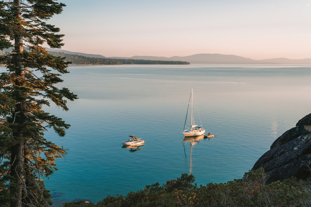 Vista vidriosa del lago Tahoe con un velero y un bote a motor en la distancia